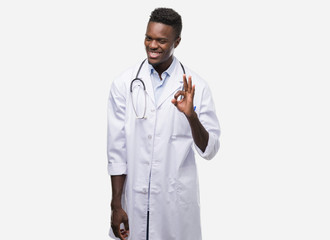 Young african american man wearing doctor coat doing ok sign with fingers, excellent symbol