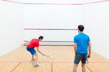Rear view of two competitive young men with a modern lifestyle playing doubles squash game on a...