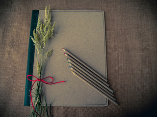 Vintage style. Organized desk with binder, dry grass, pencils and burlap background