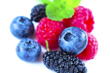 Close-up arrangement mixed, assorted berries including blackberries, strawberry, blueberry, raspberries and fresh leaf on white