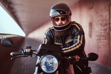 Close-up portrait of a brutal bearded biker in helmet and sunglasses dressed in a black leather...