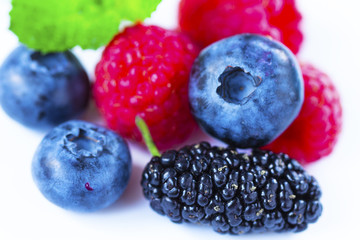 Close-up arrangement mixed, assorted berries including blackberries, strawberry, blueberry, raspberries and fresh leaf on white