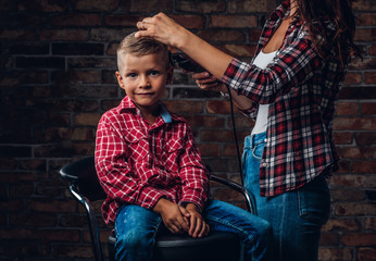 Cute preschooler boy getting haircut. Children hairdresser with trimmer is cutting little boy in a...