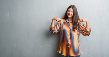 Young brunette woman over grunge grey wall looking confident with smile on face, pointing oneself with fingers proud and happy.