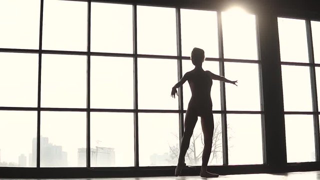 elegant ballerina is spinning on tiptoes in pointe shoes. Silhouette of ballet dancer in the studio against the background of a large window. slow motion