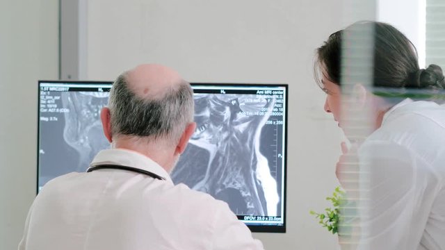 Elderly male doctor and young female nurse together look at computer x-ray of jaw and teeth. Maxillofacial surgeons examine and diagnose disease