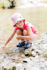 little girl crouches on the bank of a mountain stream in summer