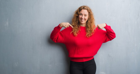 Young redhead woman over grey grunge wall wearing red sweater looking confident with smile on face, pointing oneself with fingers proud and happy.