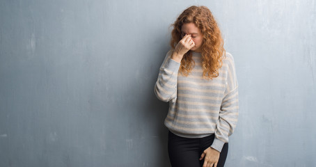 Fototapeta premium Young redhead woman over grey grunge wall tired rubbing nose and eyes feeling fatigue and headache. Stress and frustration concept.