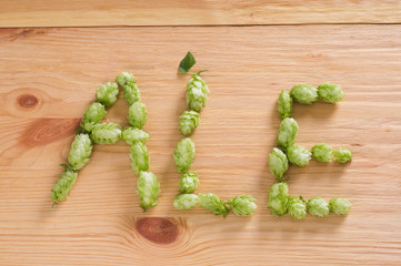 The inscription ale with hop cones on wooden background. Ingredient in beer industry. Craft beer...