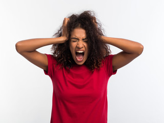 Screaming african american woman in red top with closed eyes. Depressed angry black girl over white background in studio.
