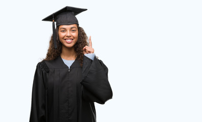 Young hispanic woman wearing graduation uniform surprised with an idea or question pointing finger with happy face, number one