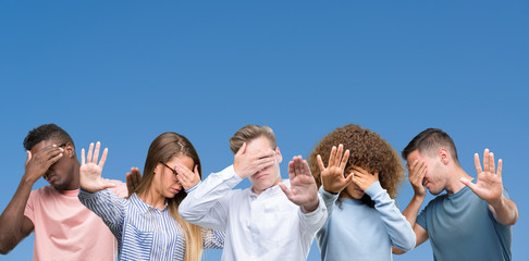Composition of group of friends over blue blackground covering eyes with hands and doing stop gesture with sad and fear expression. Embarrassed and negative concept.