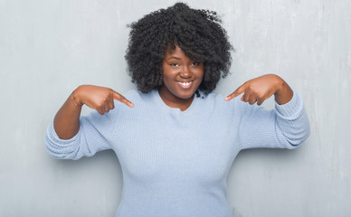 Young african american woman over grey grunge wall wearing winter sweater looking confident with...