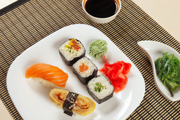 Assorted sushi, hiyashi wakame salad and soy sauce on a bamboo mat close up.