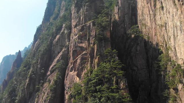 Drone aerial shot rising up over Huangshan mountain in China. Flying epic nature landscape shot of Yellow mountain. Close up of rock formations in famous tourist scenic spot.