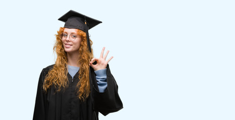 Young redhead student woman wearing graduated uniform doing ok sign with fingers, excellent symbol