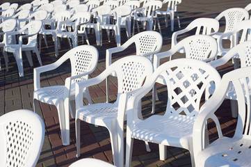 Many white plastic chairs, exposed on a Sunny day outdoors, for the event.