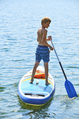 Paddle boarder. Child boy paddling on stand up paddleboard. Healthy lifestyle. Water sport, SUP surfing tour in adventure camp on active family summer beach vacation.
