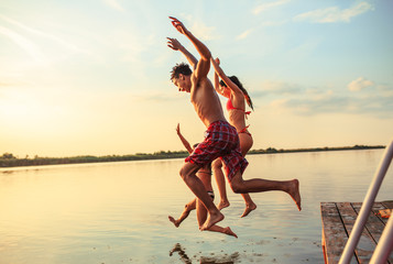 Group of friends jumping into the lake from wooden pier.Having fun on summer day. - obrazy, fototapety, plakaty