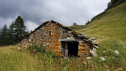 Ruiny kamiennej pokrytej porostami chaty na górskim stoku.