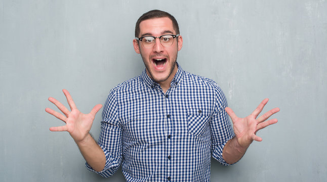 Young caucasian business man over grey grunge wall very happy and excited, winner expression celebrating victory screaming with big smile and raised hands