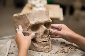 Sculptor modeling a skull out of raw clay with hands in a sculpting studio workshop