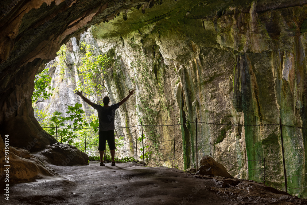 Wall mural Silueta de un hombre de pie con los brazos extendidos dentro de una cueva mirando hacia el exterior. Cueva de Zugarramurdi, España.