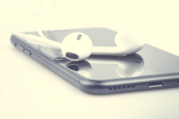 Headphones with the smartphone lie on wooden white boards. Photograph filtered in a hipster style with a shallow depth of field.