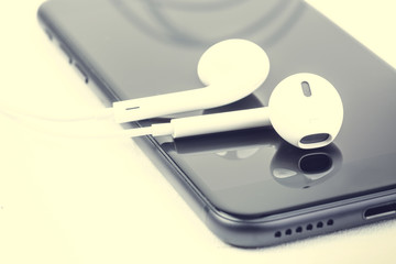 Headphones with the smartphone lie on wooden white boards. Photograph filtered in a hipster style with a shallow depth of field.