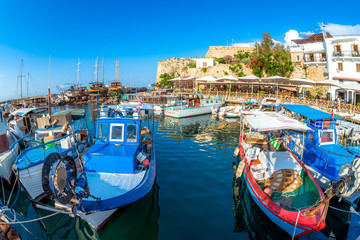 Fishing Boats moored in Kyrenia (Girne) harbour with restaurants and fortress on background - obrazy, fototapety, plakaty