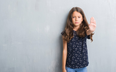 Young hispanic kid over grunge grey wall doing stop sing with palm of the hand. Warning expression...