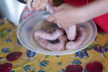 Meat grinder with fresh forcemeat and woman making sausages in kitchen