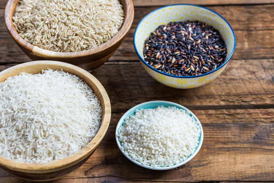 Different types of rice in wooden bowls such as basmati, brown a