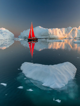 Greenland midnight Sunset iceberg mirror with red sail ship	