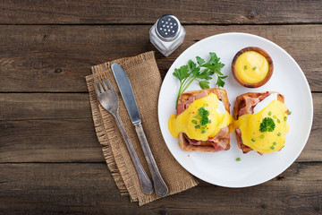 Eggs benedict with bacon on wooden background . Top view 