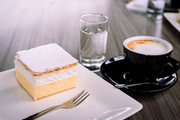 Delicious desset cream cake on the white square plate served with cappucino and water at Bled lake, Slovenia II