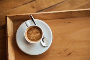 top view of white Cup with black coffee on a white saucer and teaspoon on wooden background with copyspace on the right