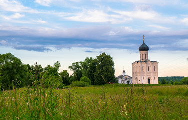 Fototapeta na wymiar Evening view through Bogolubovo meadow towards the Church of the Intercession of the Holy Virgin on the Nerl River.