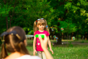 Plakat Young mother and little daughter playing in park with soap bubbles. Love family, parenthood, childhood