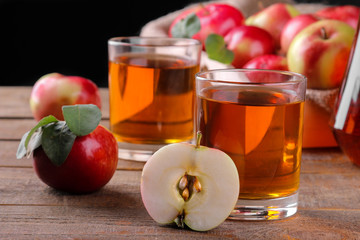 Apple juice in a glass with lots of fresh red apples on a brown wooden table on a black background