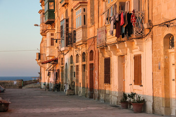 Real life on Valletta street during orange sunset - nobody on sidewalk and clothes drying on typical maltese balcony and lonely bath