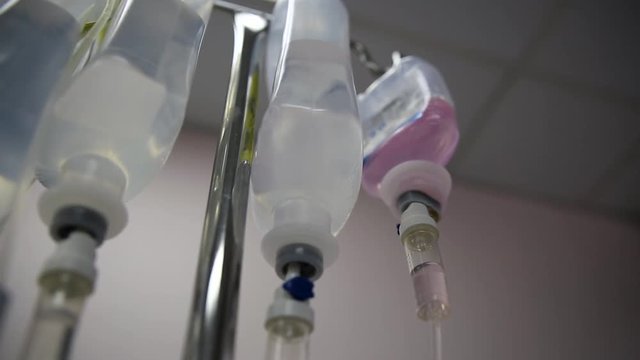 Multiple saline solution bottles hanging from pole inside a hospital.