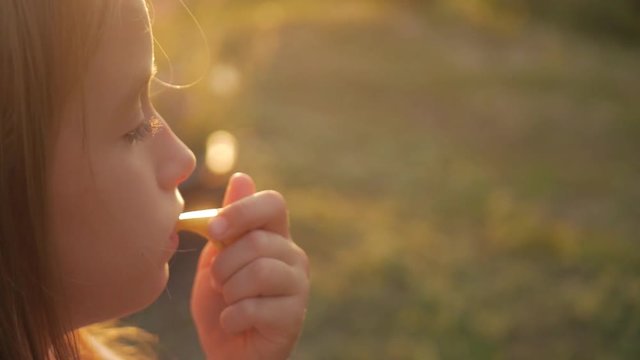 Cute teen girl blowing in whistle outdoor in nature. Close up portrait of a toddler girl blowing a toy whistle outdoors.