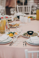 stylish wedding setting, tender pink table with wine glasses, cutlery, napkin and delicious food and drinks. luxury catering in restaurant. modern wedding reception