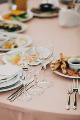 stylish wedding setting, tender pink table with wine glasses, cutlery, napkin and delicious food and drinks. luxury catering in restaurant. modern wedding reception