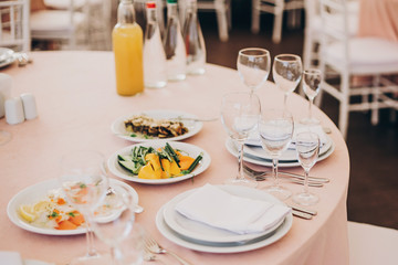 stylish wedding setting, tender pink table with wine glasses, cutlery, napkin and delicious food and drinks. luxury catering in restaurant. modern wedding reception
