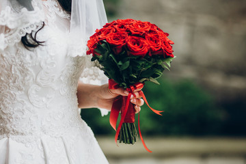 beautiful bride holding stylish bouquet in the morning. red roses wedding bouquet