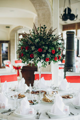 stylish wedding table setting. elegant wedding table with red roses decoration and white silk chairs and napkins. luxury catering in restaurant for wedding reception