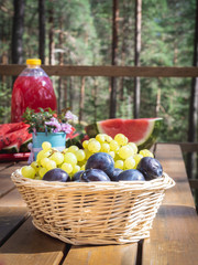 Closeup of basket with grapes and plumps on a wooden table, outdoor party or picnic